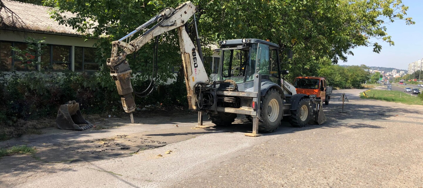Backhoe loader with hydraulic breaker performing roadwork, depicting construction activity on a linear asset for AP Sensing monitoring Backhoe loader with hydraulic breaker performing roadwork, depicting construction activity on a linear asset for AP Sensing monitoring